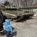 Seorang warga lokal berjalan dengan seorang anak melewati tank pasukan pro-Rusia di kota Mariupol, Ukraina, Jumat, 18 Maret 2022. (Foto Reuters via BBC)