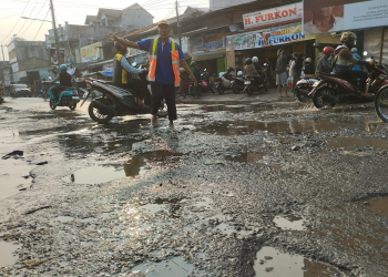 Seorang tukang parkir yang membantu mengatur lalu lintas di tengah jalanan yang rusak dan tergenang air di Pasar Rau, Minggu (25/6).// BANTEN POS// EDWIN